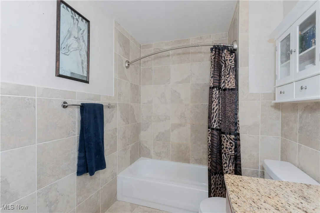 Bathroom with tile walls, shower / bath combination with curtain, and vanity