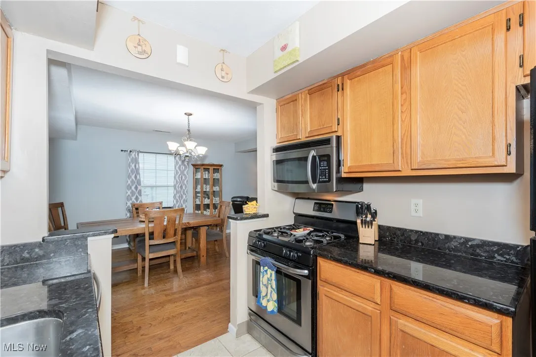 Kitchen with stainless steel appliances, decorative light fixtures, dark stone countertops, a chandelier, and light wood-style flooring