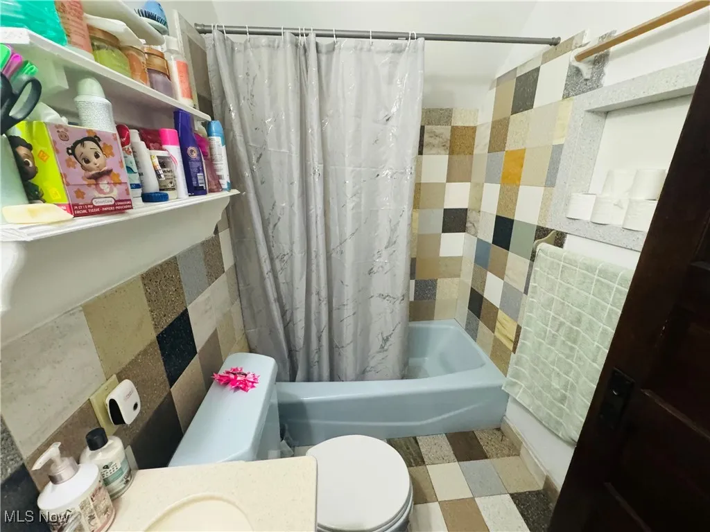Full bathroom with shower / bathtub combination with curtain, tile patterned floors, vanity, and tile walls