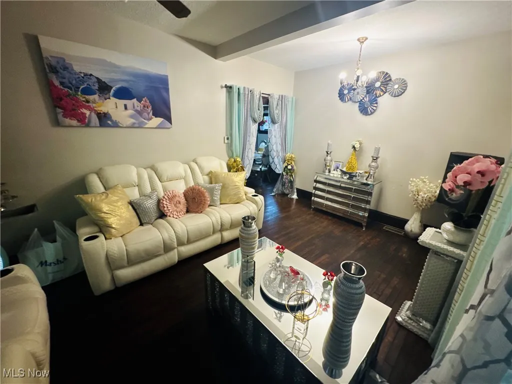Living room featuring dark wood-style flooring, beamed ceiling, and a chandelier
