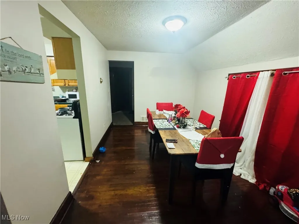 Dining area with a textured ceiling, dark wood finished floors, and lofted ceiling