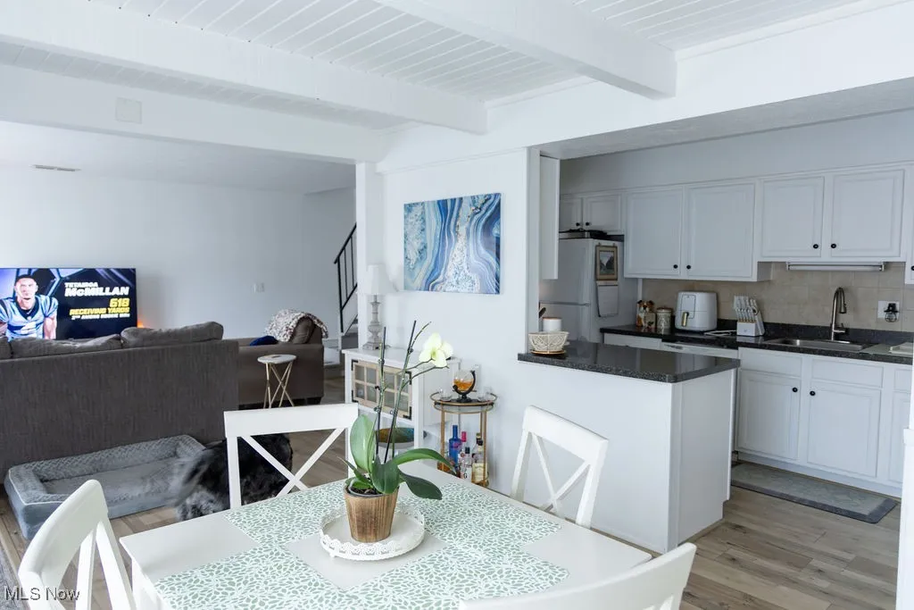 Dining area featuring light wood finished floors, beamed ceiling, and stairs