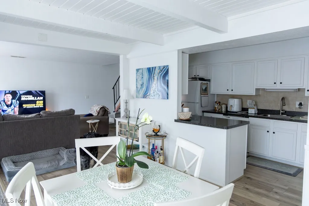 Dining room featuring light wood-style flooring, beam ceiling, and stairway
