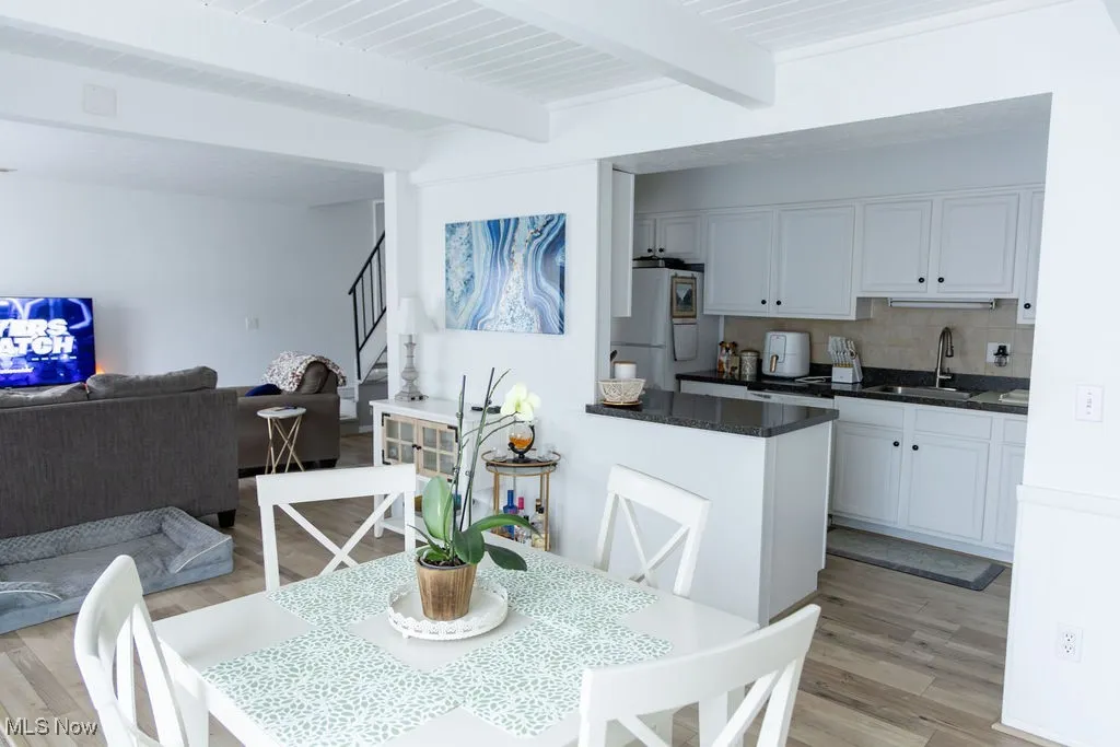 Dining room featuring light wood finished floors, beamed ceiling, and stairs