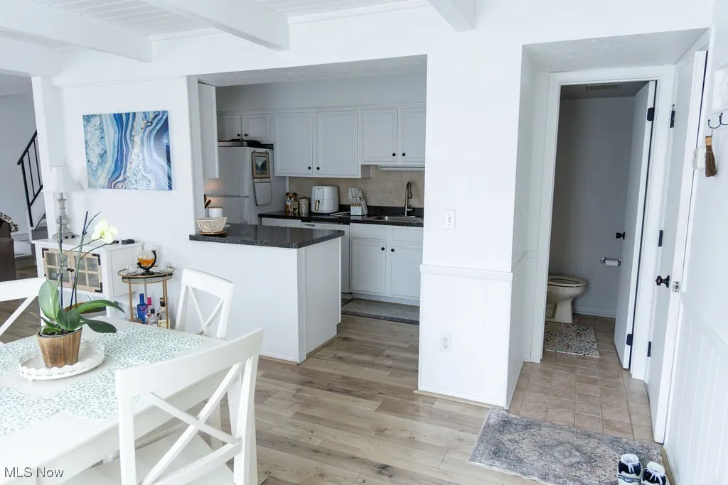 Kitchen featuring beam ceiling, white cabinetry, tasteful backsplash, light wood-style flooring, and dark stone countertops