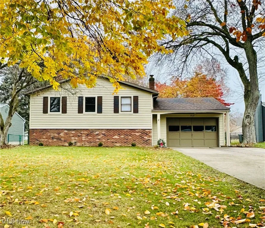 View of front facade with a garage, brick siding, a chimney, concrete driveway, and a front yard