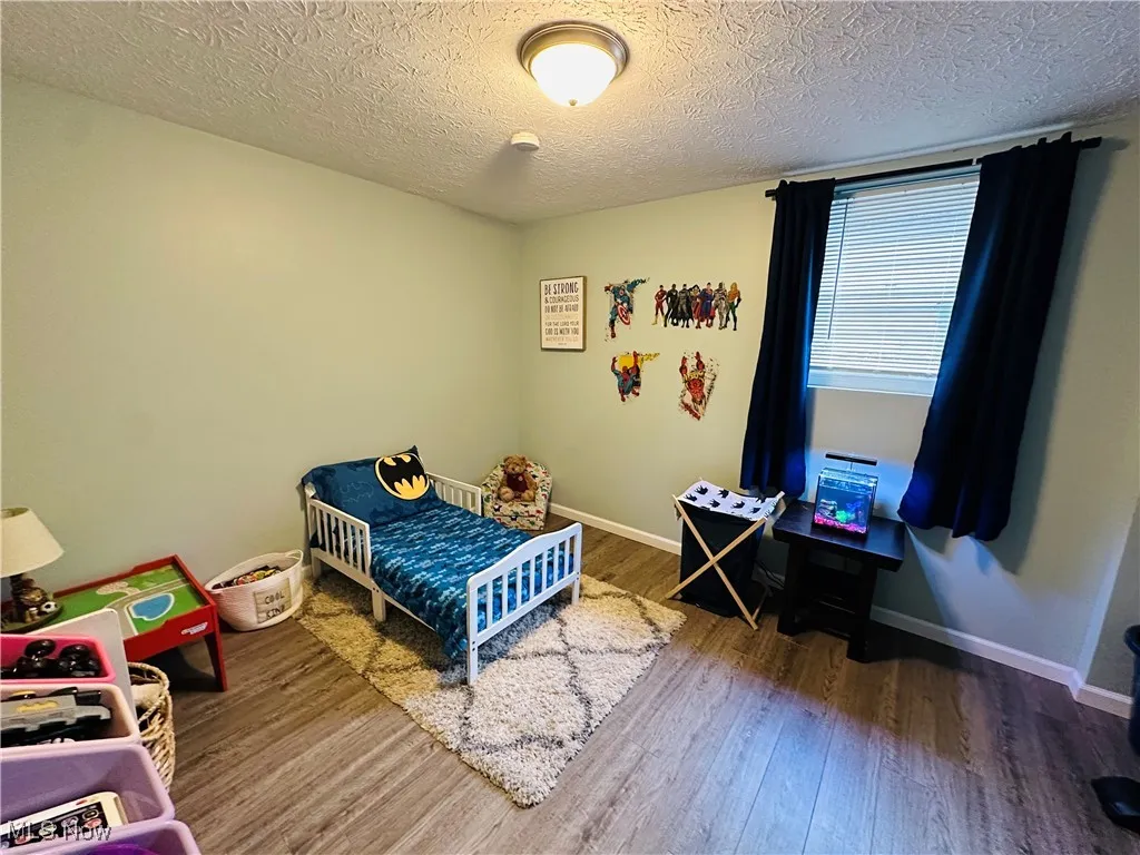 Bedroom with a textured ceiling, wood finished floors, and a nursery area