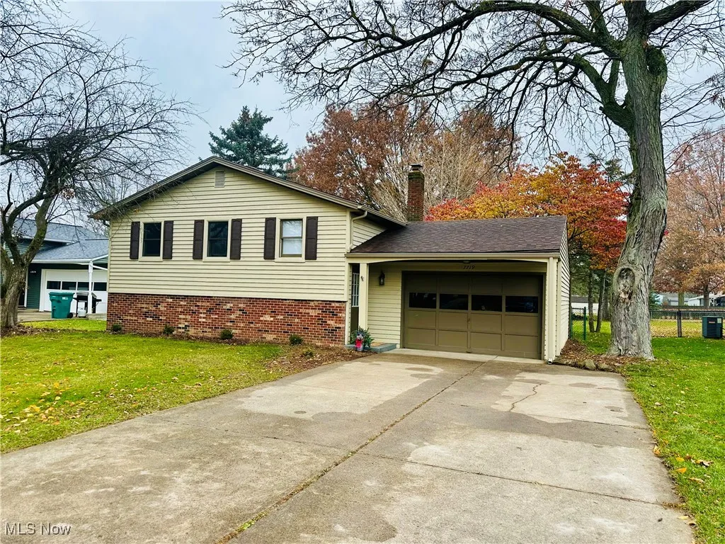 Split level home with a front yard, concrete driveway, a chimney, and an attached garage
