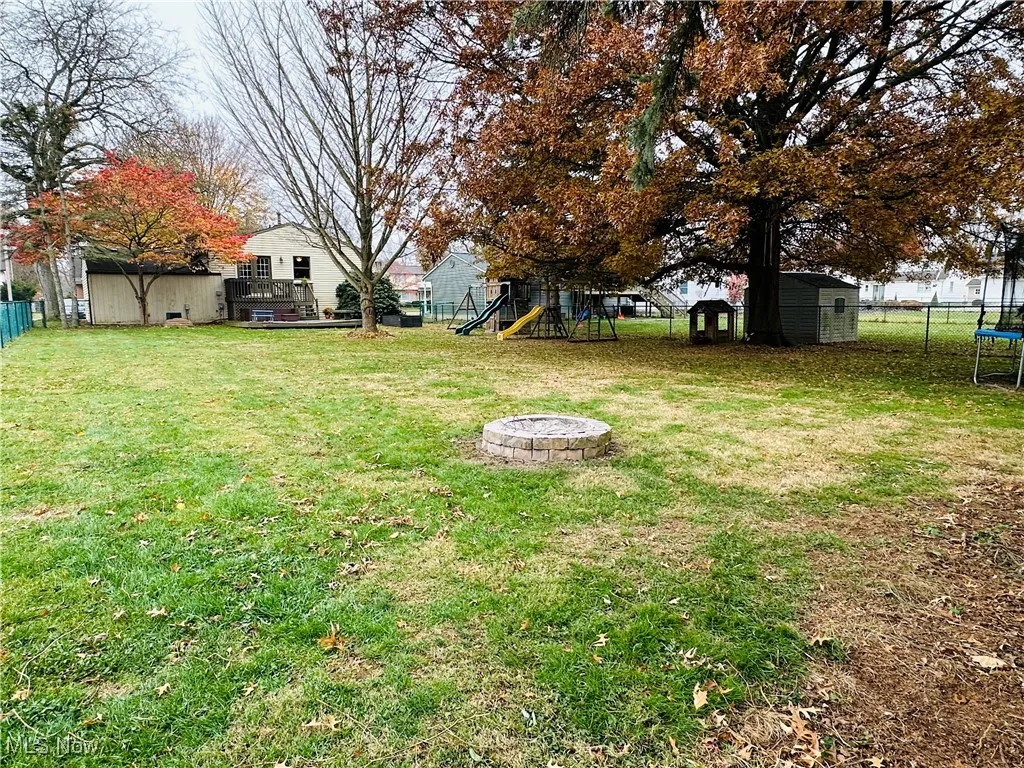 Fenced backyard featuring an outdoor fire pit, a playground, a shed, and a trampoline