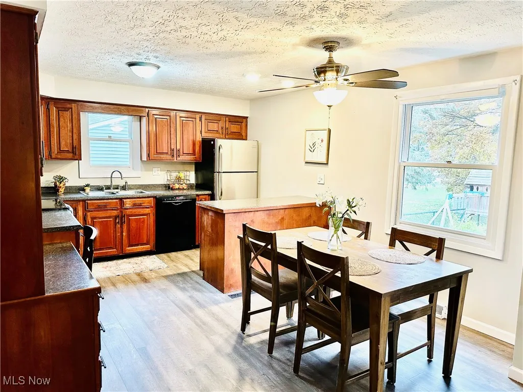 Kitchen featuring brown cabinetry, freestanding refrigerator, a textured ceiling, black dishwasher, and dark countertops