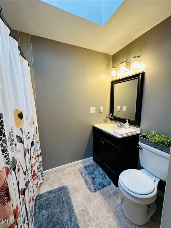 Full bath with curtained shower, a skylight, vanity, and light tile patterned flooring
