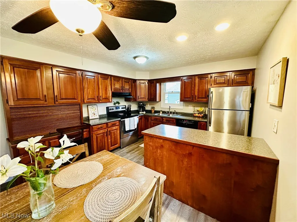Kitchen with stainless steel appliances, a ceiling fan, a textured ceiling, dark countertops, and brown cabinets