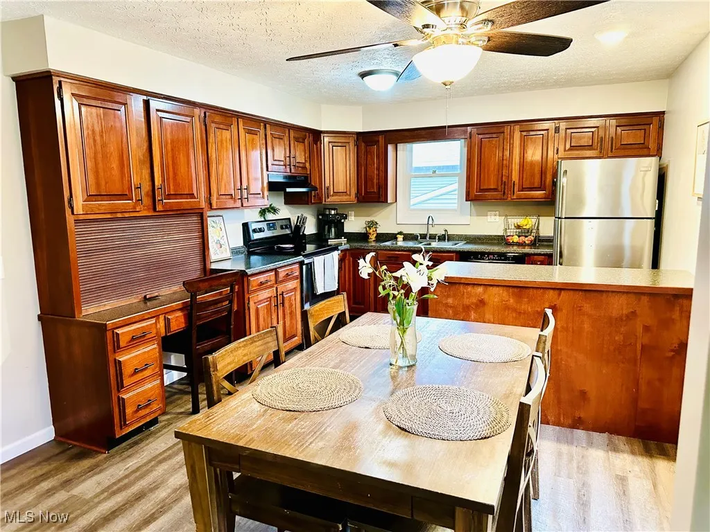 Kitchen with dark countertops, brown cabinets, freestanding refrigerator, range with electric cooktop, and a textured ceiling