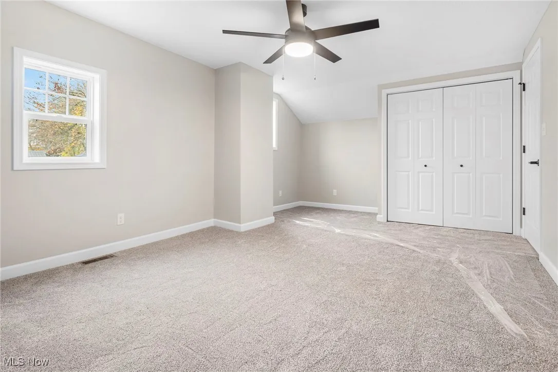 Unfurnished bedroom with a closet, light carpet, vaulted ceiling, and ceiling fan