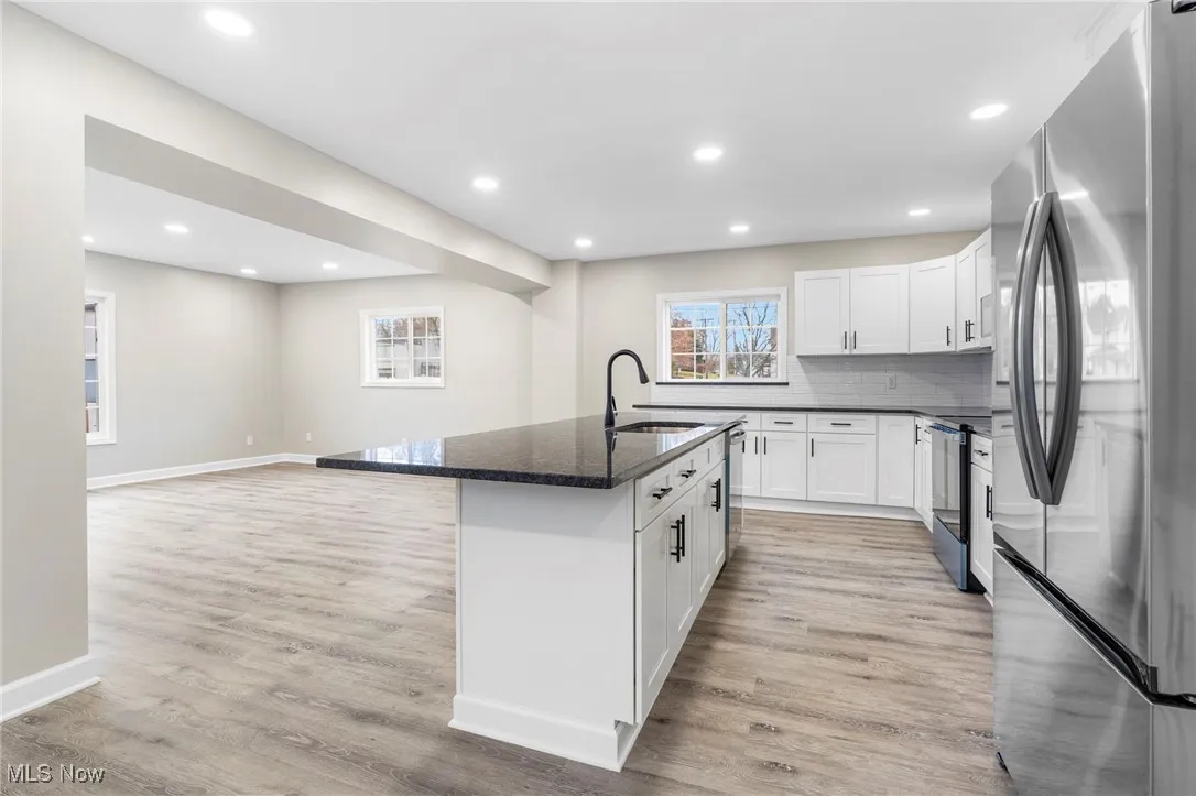 Kitchen with stainless steel appliances, open floor plan, a kitchen island with sink, dark stone countertops, and white cabinets