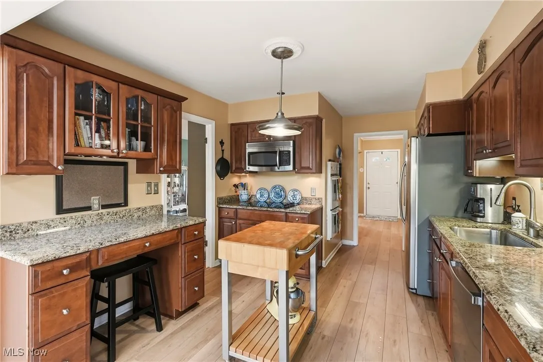 Kitchen with light stone counters, decorative light fixtures, stainless steel appliances, glass insert cabinets, and light wood finished floors