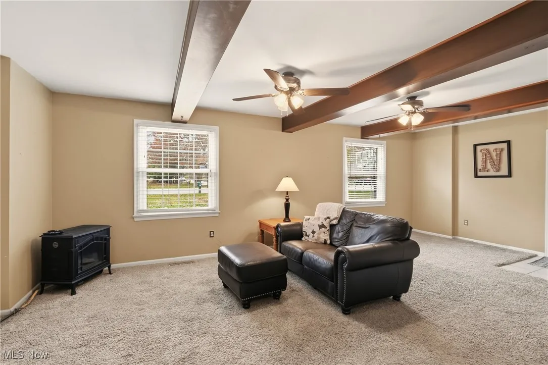 Living room with carpet floors, beamed ceiling, ceiling fan, and a wood stove