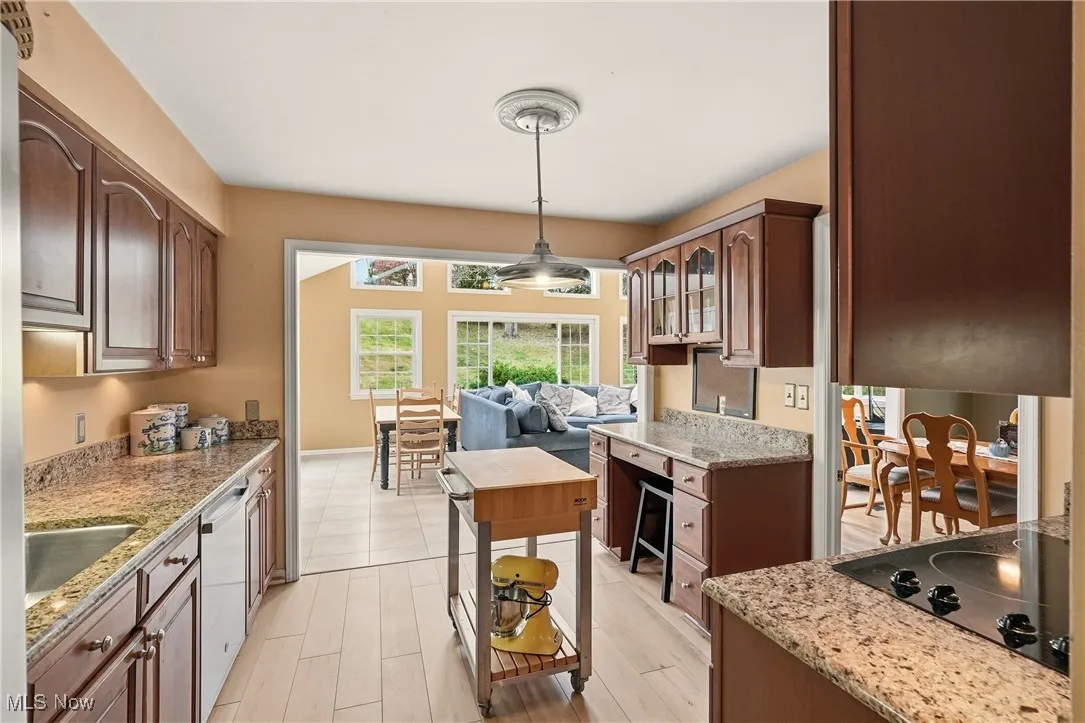 Kitchen with light stone countertops, black electric cooktop, dishwasher, pendant lighting, and glass insert cabinets