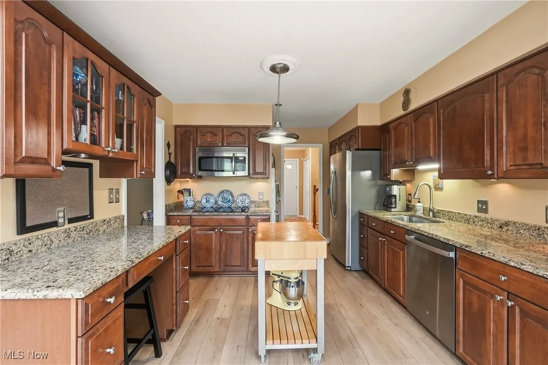 Kitchen featuring hanging light fixtures, light stone counters, appliances with stainless steel finishes, glass insert cabinets, and light wood-type flooring