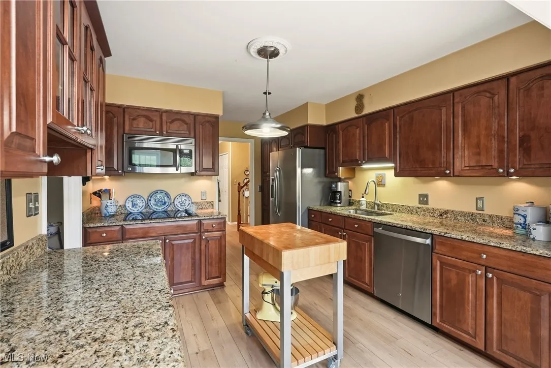 Kitchen with pendant lighting, stainless steel appliances, light stone countertops, and light wood finished floors