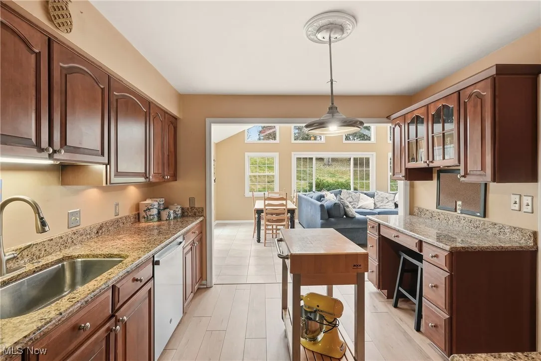 Kitchen featuring light stone counters, open floor plan, dishwashing machine, and decorative light fixtures