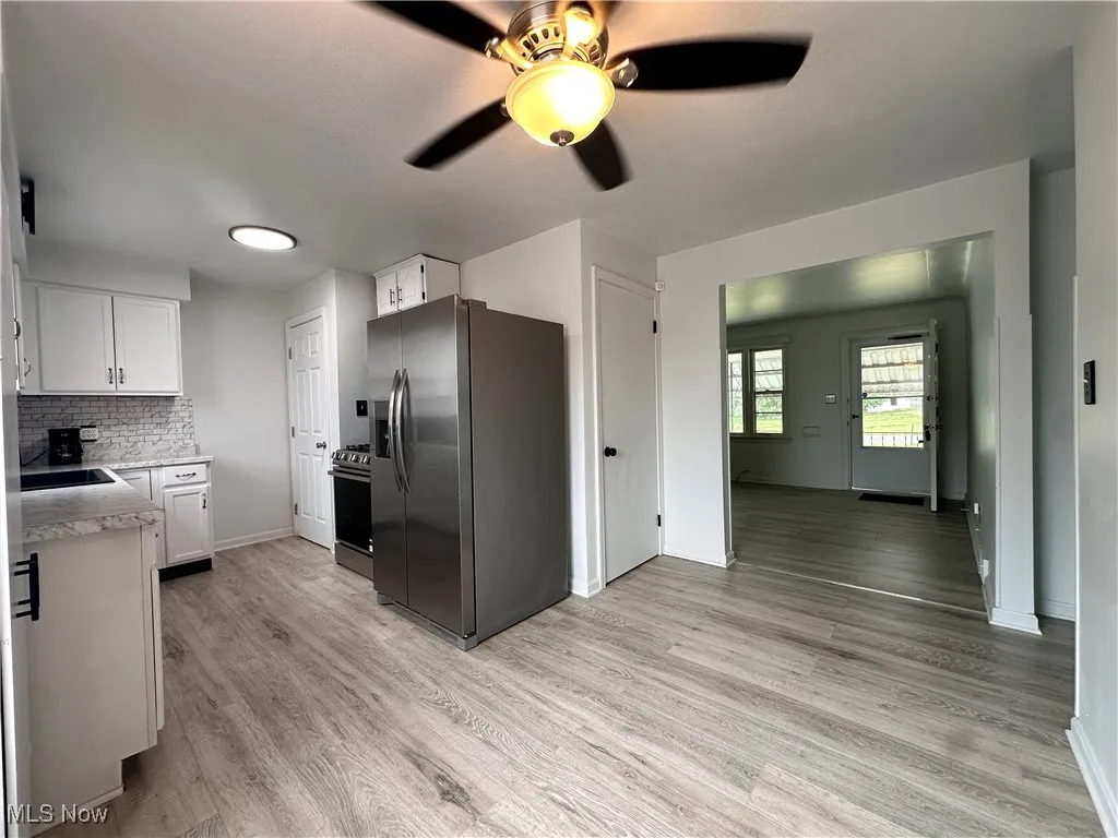 Kitchen featuring white cabinetry, ceiling fan, appliances with stainless steel finishes, light hardwood / wood-style flooring, and backsplash