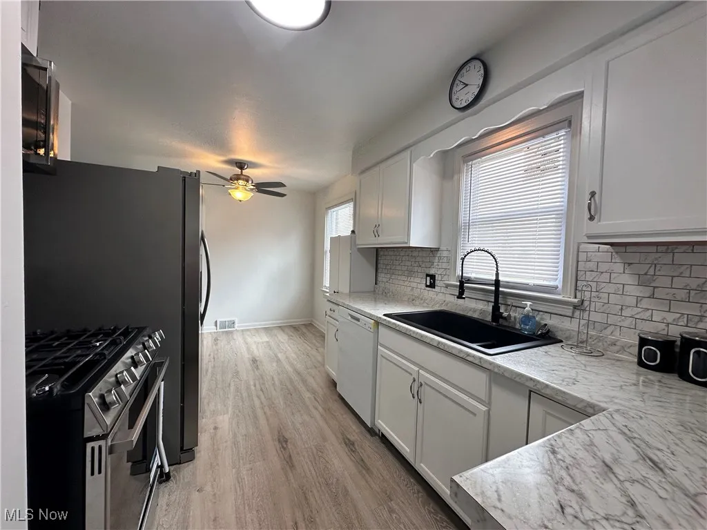 Kitchen featuring tasteful backsplash, stainless steel stove, sink, light wood-type flooring, and ceiling fan