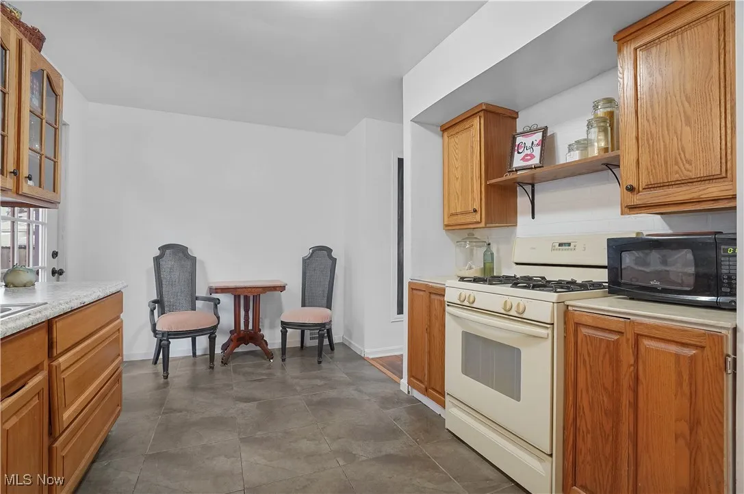 Kitchen with brown cabinetry, white gas range oven, light countertops, and black microwave