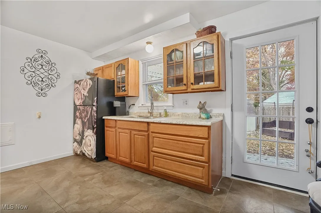 Kitchen featuring glass insert cabinets, freestanding refrigerator, brown cabinetry, and light stone countertops