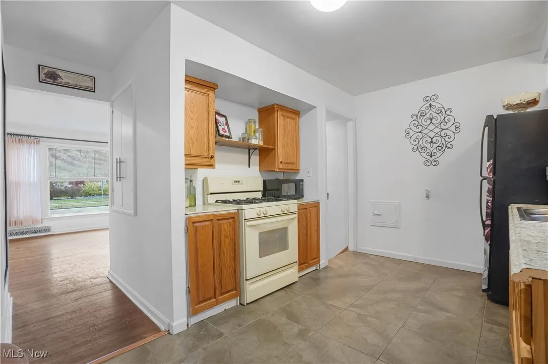 Kitchen featuring black appliances, light countertops, brown cabinetry, and open shelves