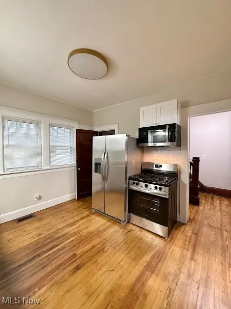 Kitchen featuring appliances with stainless steel finishes, decorative backsplash, white cabinetry, and light wood-style flooring