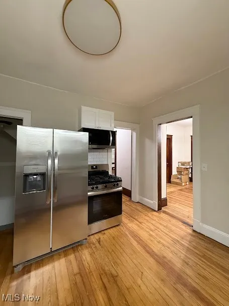 Kitchen featuring appliances with stainless steel finishes, white cabinets, light wood finished floors, and backsplash