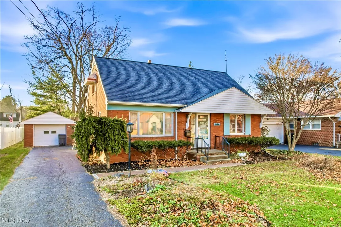 View of front of property with an outbuilding, a shingled roof, brick siding, and asphalt driveway