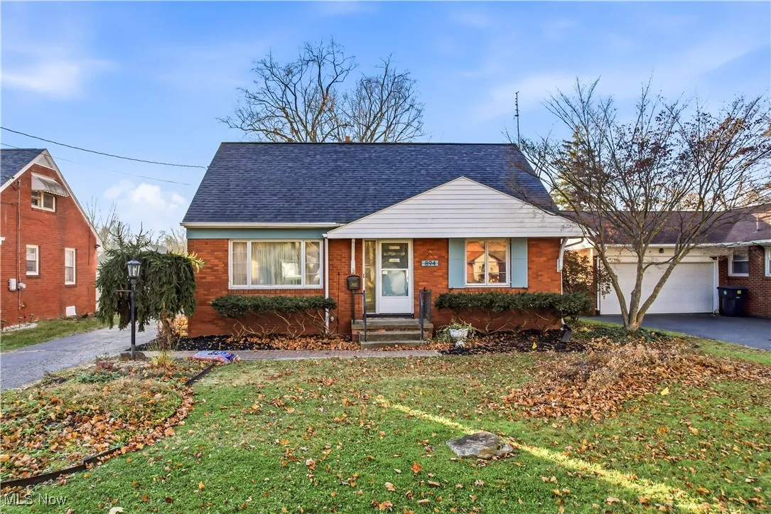 Bungalow-style home with driveway, brick siding, a front lawn, an attached garage, and a shingled roof