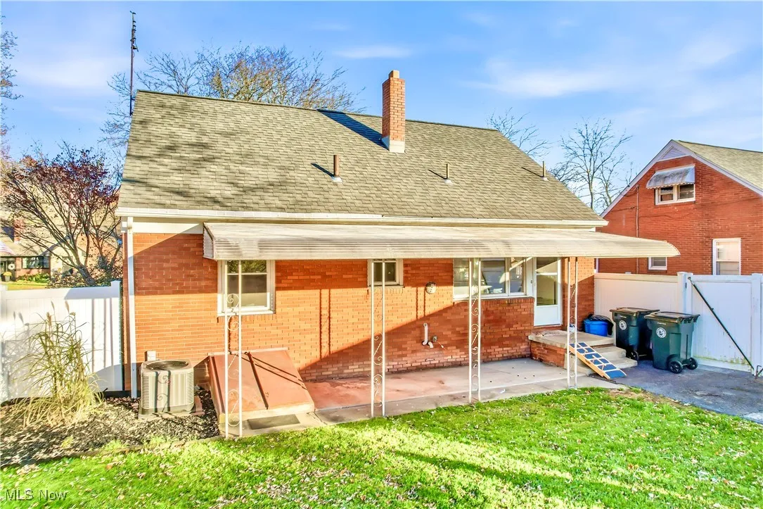 Rear view of house with a chimney, a patio, roof with shingles, and brick siding