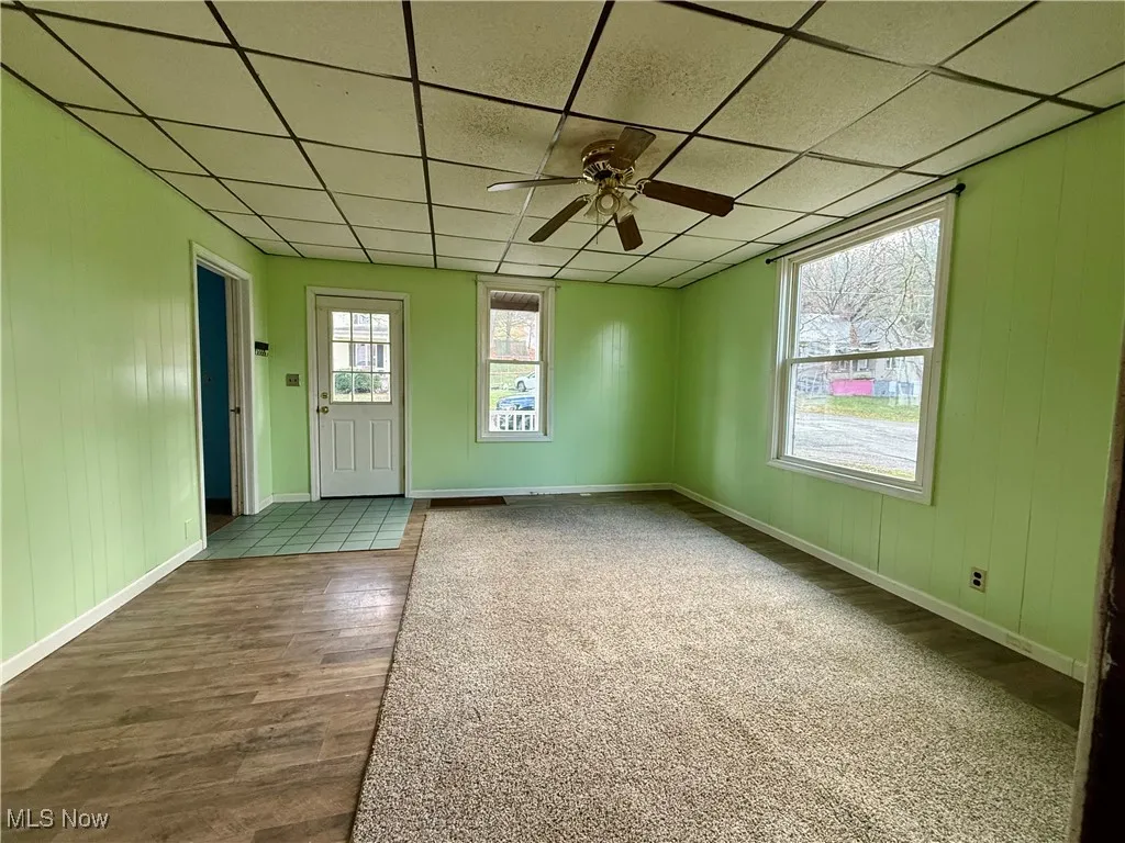 Empty room featuring a paneled ceiling, a ceiling fan, wood finished floors, and wood walls