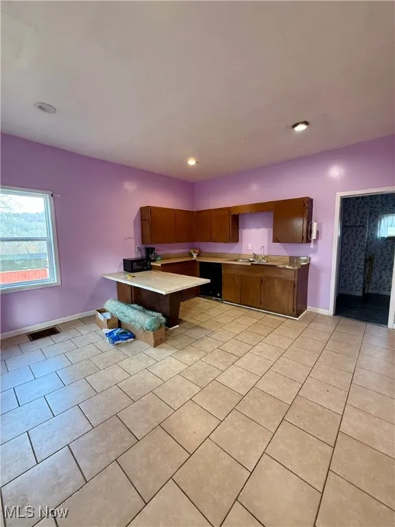 Kitchen featuring light countertops, a peninsula, black appliances, a kitchen breakfast bar, and brown cabinetry