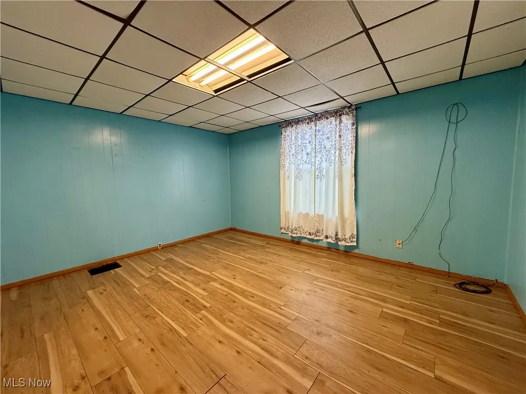 Unfurnished room featuring a drop ceiling, light wood finished floors, and wood walls
