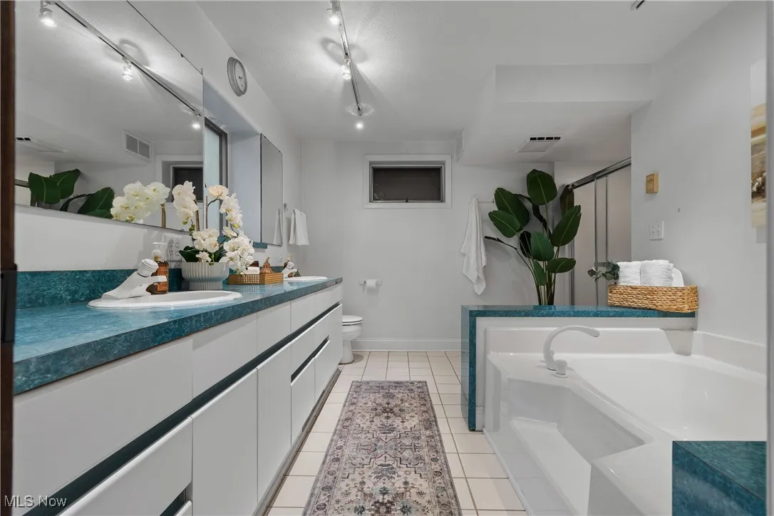 Bathroom with double vanity, light tile patterned floors, a garden tub, and a stall shower