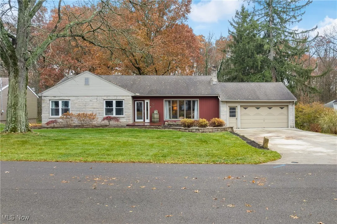 Single story home with concrete driveway, a chimney, a front lawn, a garage, and stone siding