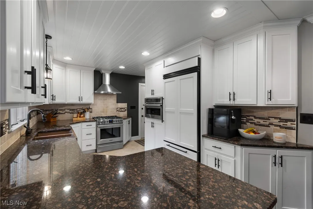 Kitchen featuring dark stone countertops, white cabinetry, stainless steel appliances, decorative backsplash, and recessed lighting