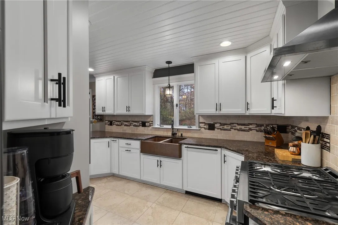 Kitchen with wall chimney exhaust hood, gas stove, white cabinetry, and recessed lighting
