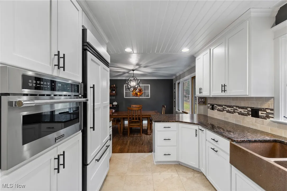 Kitchen with ornamental molding, white cabinets, oven, tasteful backsplash, and pendant lighting