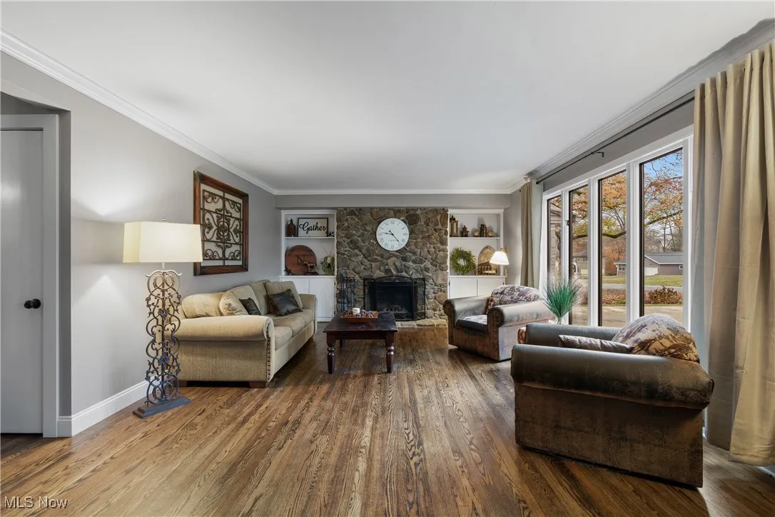 Living room with a fireplace, built in shelves, wood finished floors, and ornamental molding