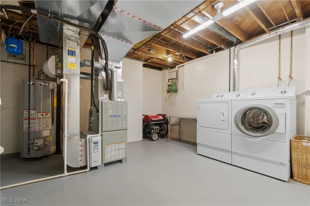 Unfinished below grade area with water heater, heating unit, and independent washer and dryer