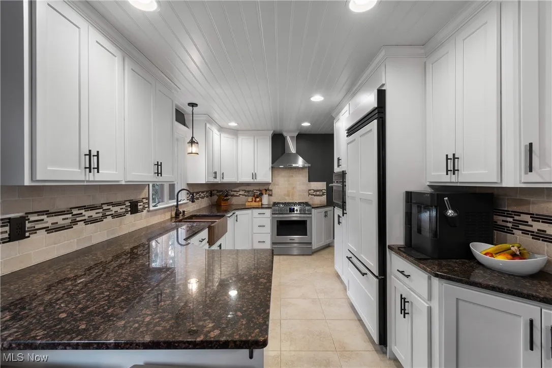 Kitchen featuring dark stone countertops, white cabinets, a peninsula, pendant lighting, and stainless steel range with gas stovetop