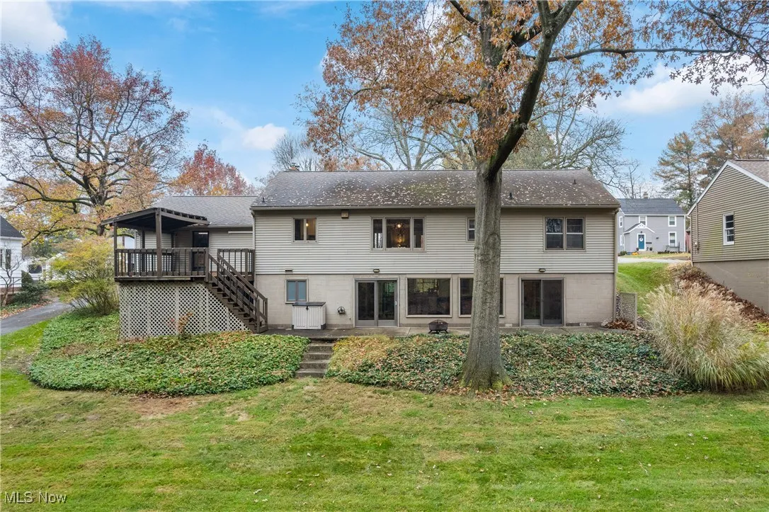Back of property featuring stairway, a lawn, a deck, a patio area, and roof with shingles