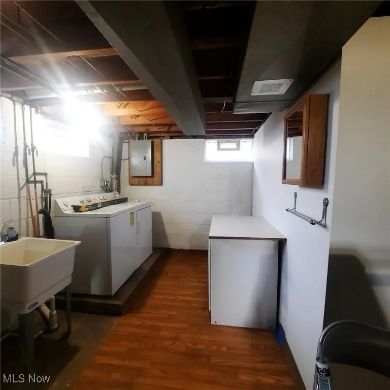 Laundry room featuring dark wood-style vinyl flooring, electric panel, glass block vented window and GE Washer and Dryer, Sink and folding counter/cabinet.