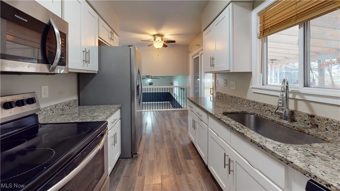 Kitchen with appliances with stainless steel finishes, light stone countertops, a ceiling fan, white cabinets, and dark wood-style flooring