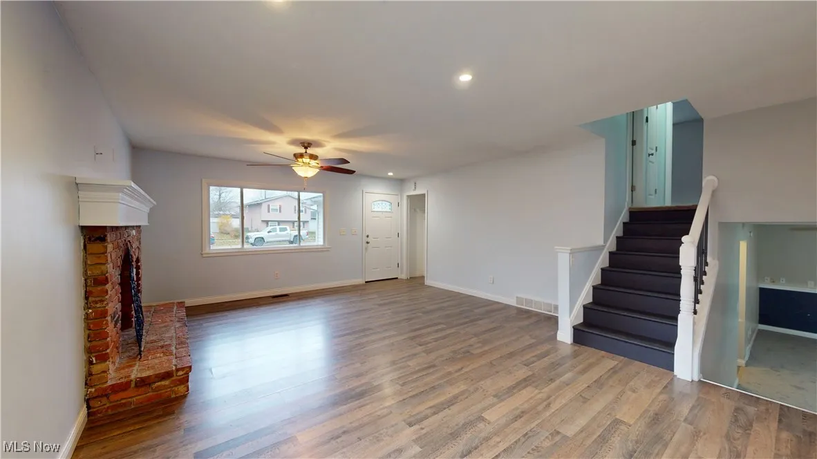 Unfurnished living room featuring a fireplace, wood finished floors, ceiling fan, stairway, and recessed lighting